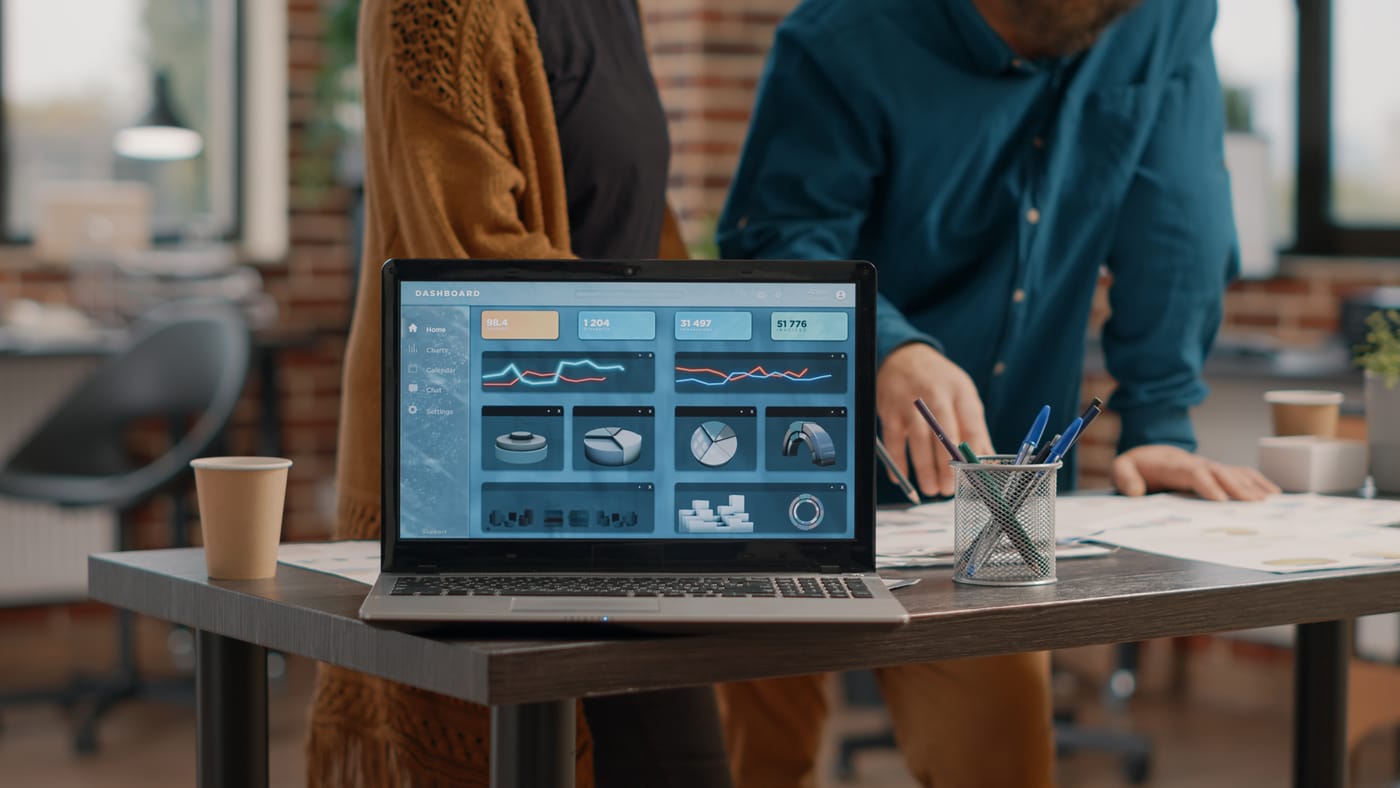 Two colleagues reviewing a software analytics dashboard on a laptop in a modern office